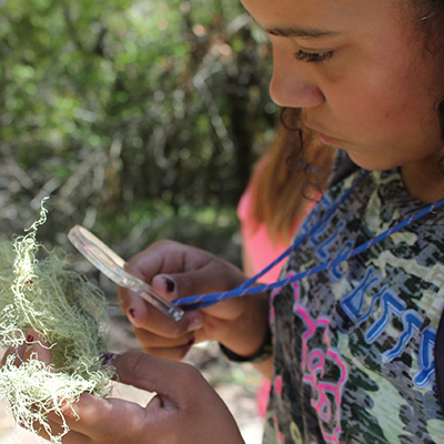 A student is outdoors examining nature through a hand lens